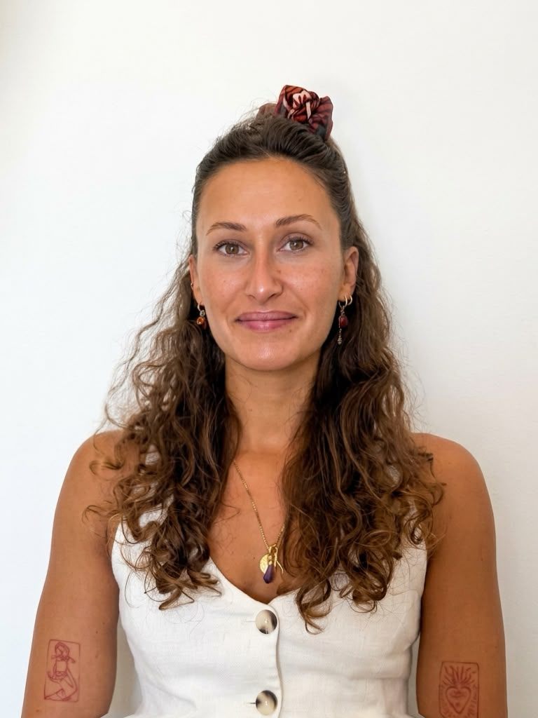 Ritratto di Lisa Bignone sorridente, con i capelli ricci e un top bianco, davanti a una parete chiara